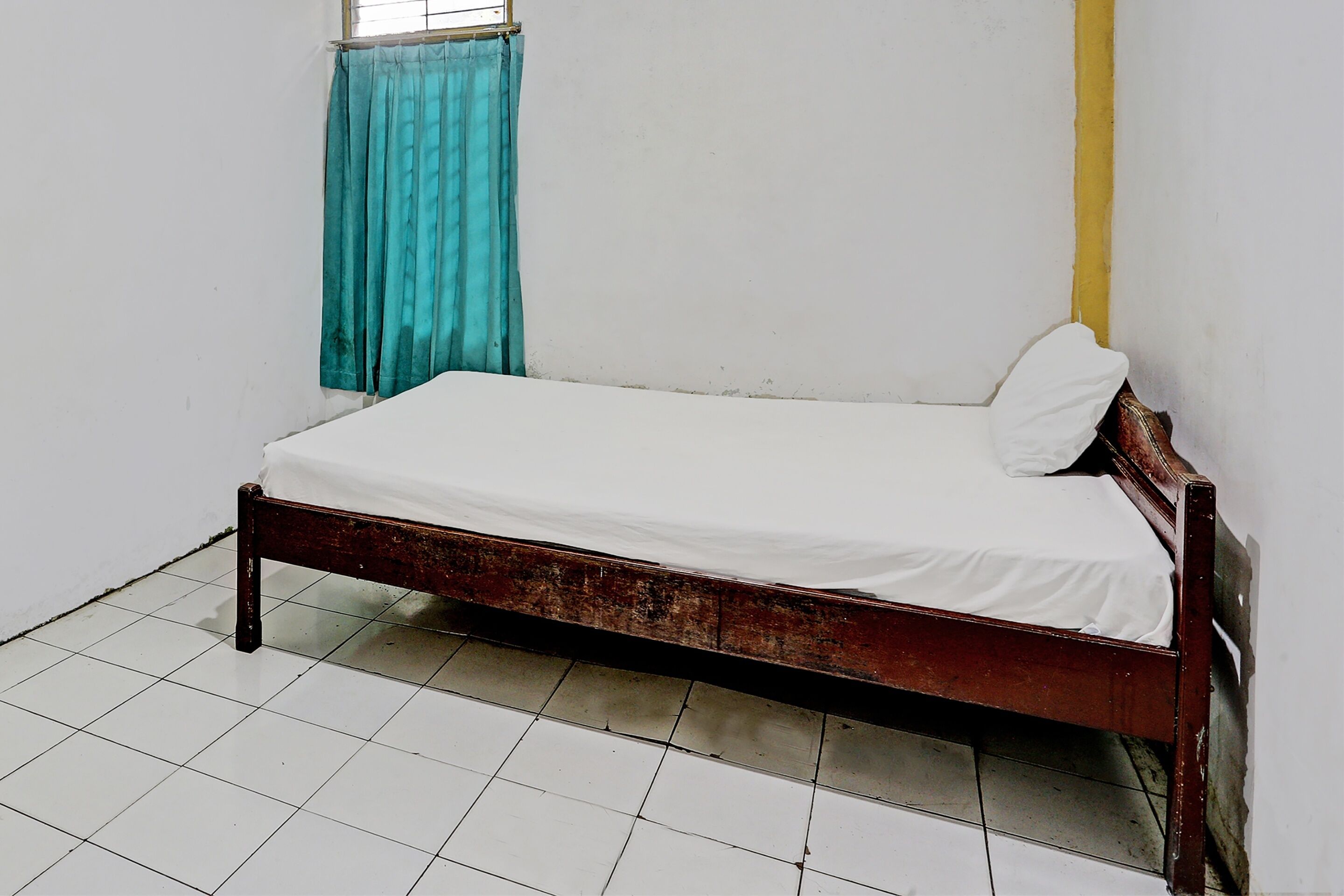 Una cama individual en una habitación con suelo de baldosas blancas y una ventana con cortinas azules.