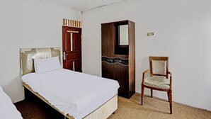 A bedroom with a single bed, a wooden wardrobe, a chair, and a door.