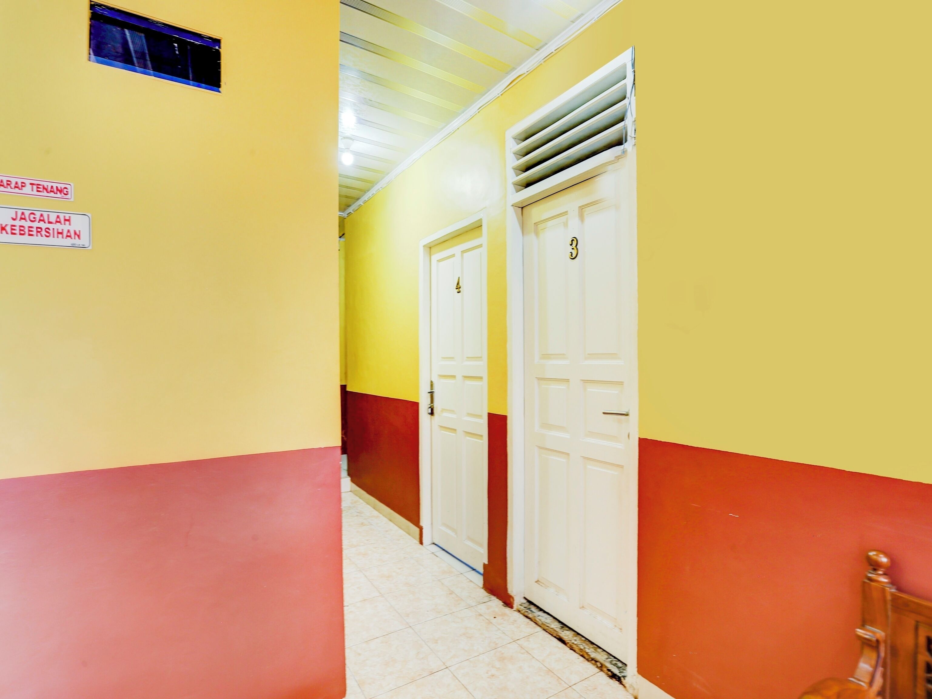 A hallway with yellow and red walls, two white doors, and a vent on the ceiling.