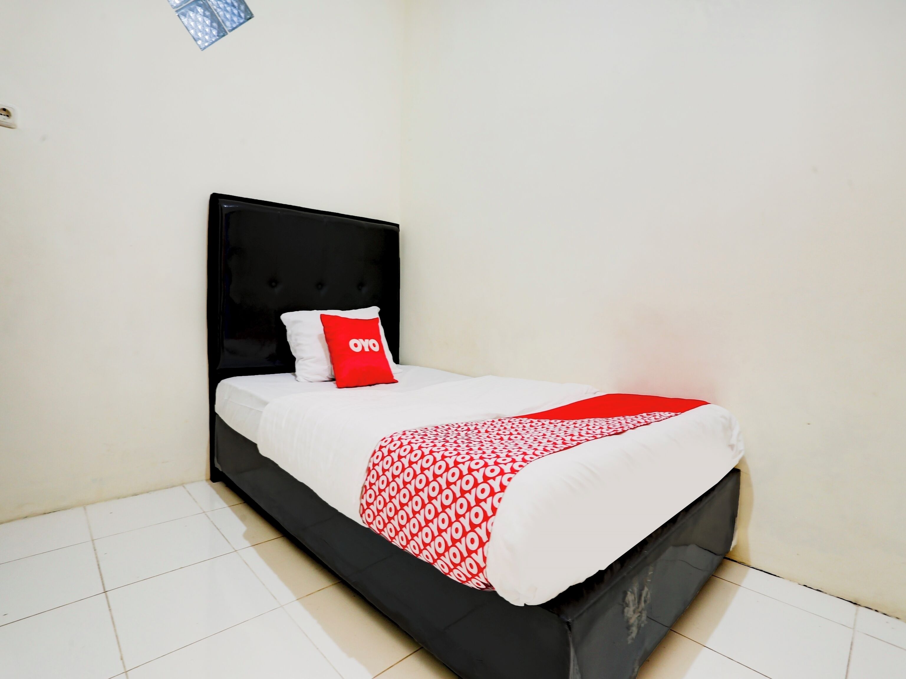 A bed with a black headboard, white bedding, and a red pillow with "OYO" text.