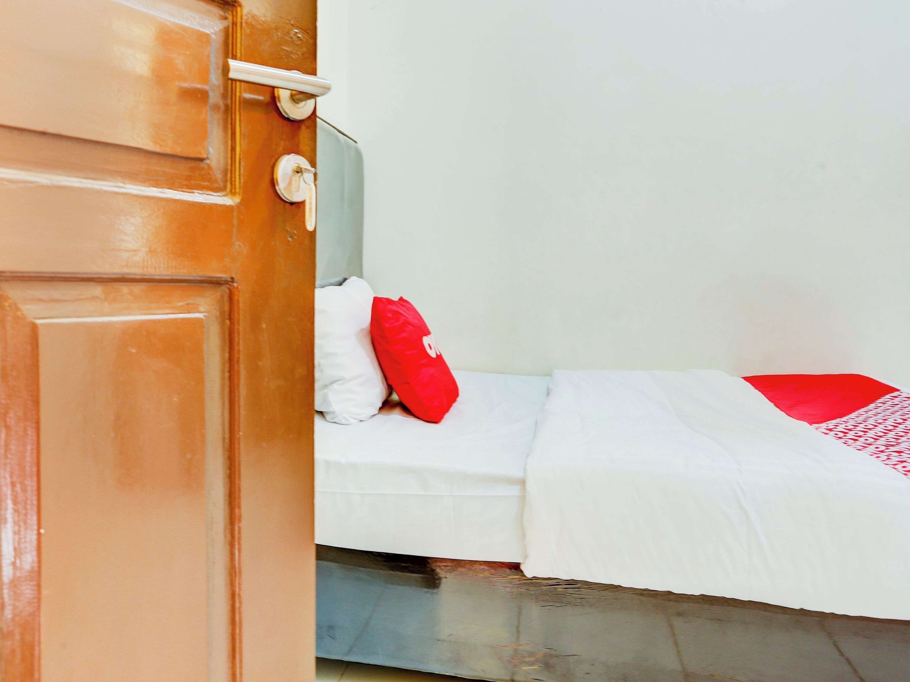 A room with a bed, a red pillow, and a white blanket.