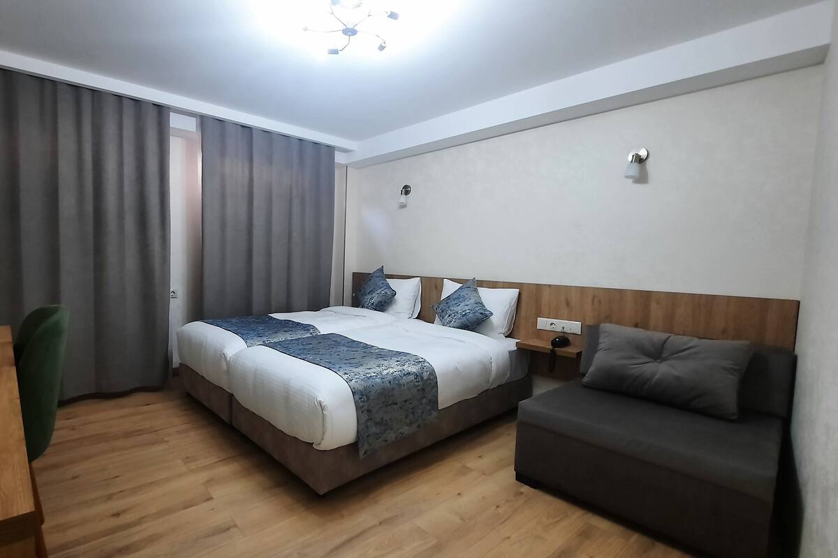 A hotel room with a bed, a desk, a chair, and a sofa.