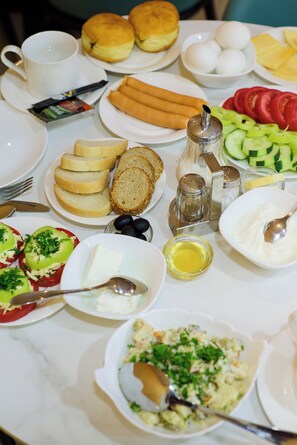 A breakfast table with various food items including bread, eggs, tomatoes, and olives.