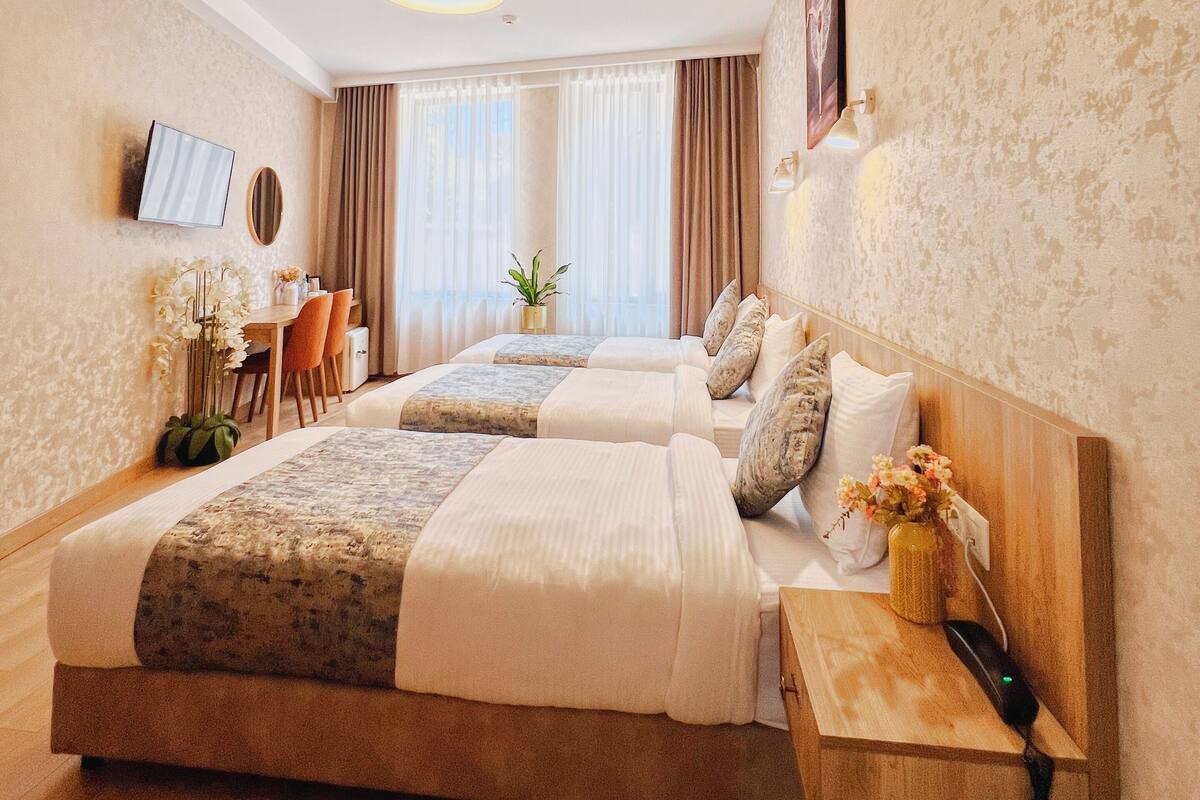 A hotel room with two beds, a desk, a chair, a TV, and a window with curtains.