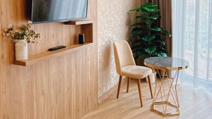 A modern living room with a flat-screen TV mounted on a wooden wall, a comfortable chair, a small round table, and a large potted plant. - Hotel DownTown Avlabari (Tbilisi)