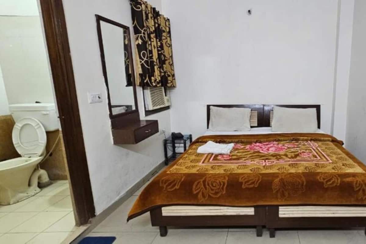 A bedroom with a bed, a bedside table, a mirror, a toilet, and a chair.
