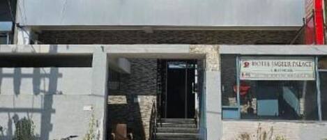 Un edificio moderno con fachada de vidrio y un letrero que indica el nombre del hotel, “Hotel Ayer Palace”.