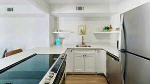Une cuisine moderne avec des meubles blancs, un réfrigérateur en acier inoxydable, un four encastré et une table à manger en verre.