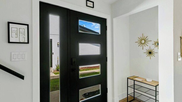 Une porte noire avec une fenêtre, une petite étagère sur laquelle se trouve un bol, et un plan architectural encadré accroché au mur.