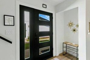 Una puerta negra con un ventanal, un estante pequeño con un cuenco y un dibujo arquitectónico enmarcado en la pared.