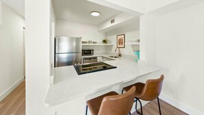 Una cocina moderna con un refrigerador de acero inoxidable, un microondas y un lavamanos. Hay dos sillas marrones en la encimera.