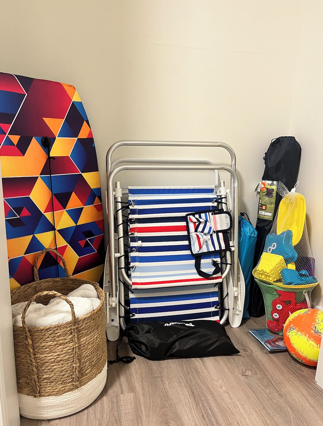 Een kamer met een metalen bedframe, een wand met een kleurrijk geometrisch patroon, een rieten mand met een witte handdoek en een zwarte trekkoordtas.