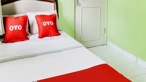 A bed with white bedding and two red pillows with "OYO" text, a wooden headboard, a white door, and green walls. - OYO 90204 Surya Inn Syariah (Cikarang)