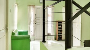 A room with a green sofa, a white door, and a staircase with a black railing. - OYO 90204 Surya Inn Syariah (Cikarang)