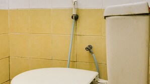 A toilet with a yellow-tiled wall and a blue pipe. - OYO 90204 Surya Inn Syariah (Cikarang)