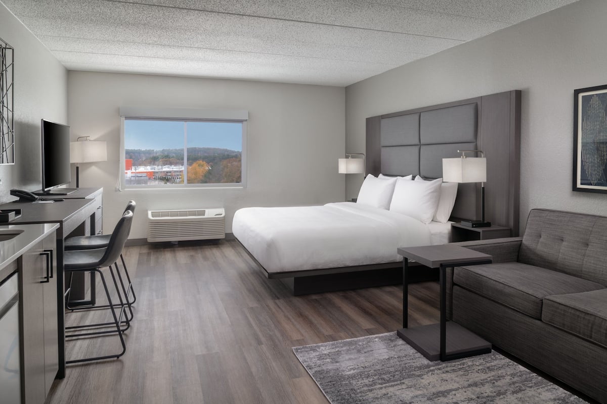 Una habitación de hotel moderna con una cama grande, un escritorio con una silla, un sofá y un ventanal con vistas al exterior.