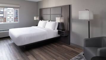 A modern hotel room with a large bed, bedside lamps, a chair, and a view of buildings through the window.