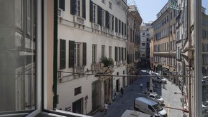 A narrow street with buildings on both sides, a few pedestrians, and parked vehicles.