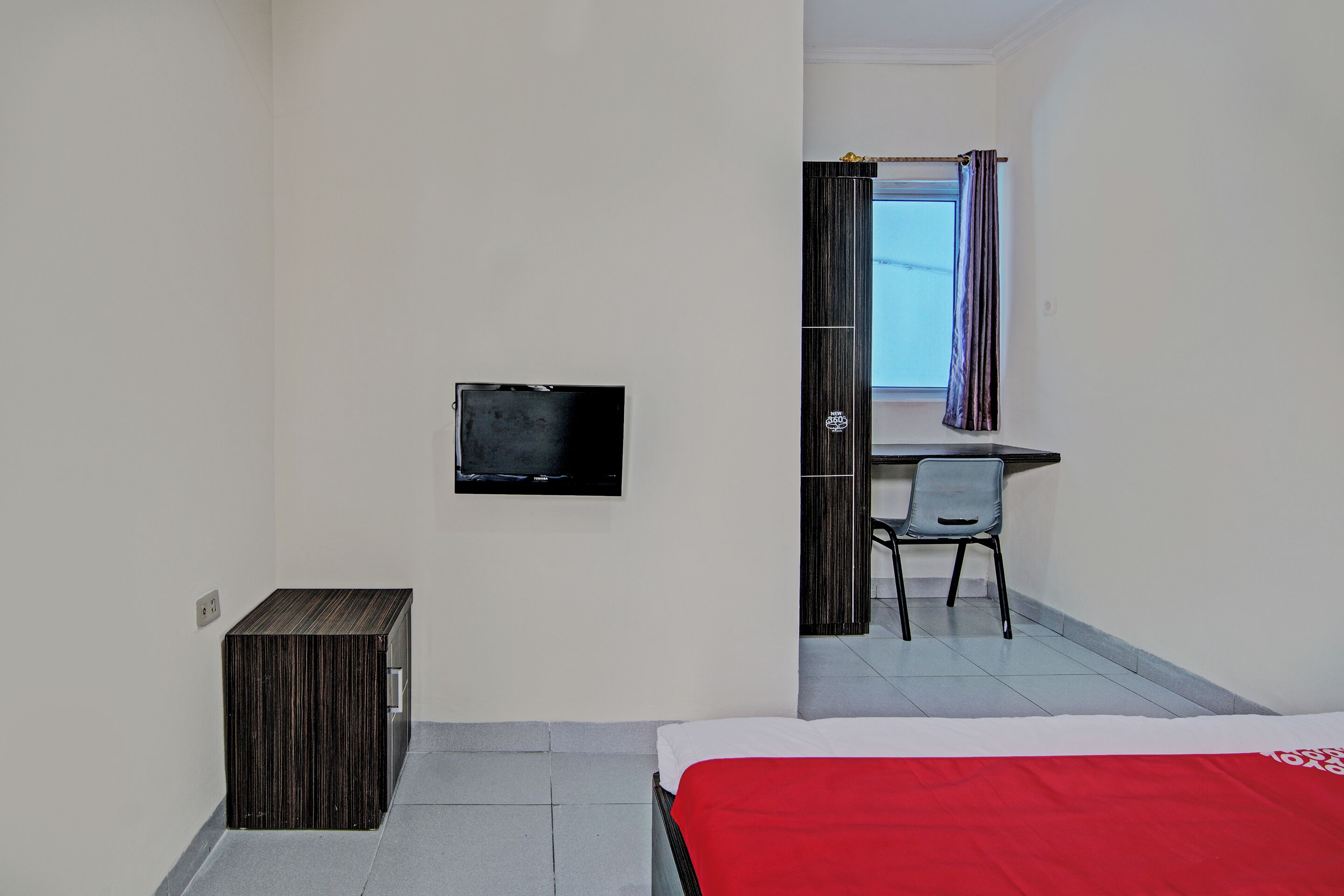 Quarto de hotel com uma cama, uma televisão, uma escrivaninha e uma cadeira.