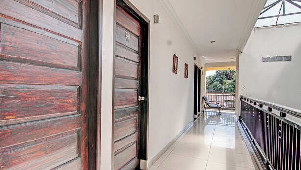 A corridor with wooden doors, a tiled floor, and a balcony with a railing. - Hotel O Rosela House Syariah (Pekanbaru)