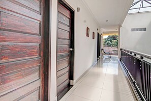 A corridor with wooden doors, a tiled floor, and a balcony with a railing. - Hotel O Rosela House Syariah (Pekanbaru)