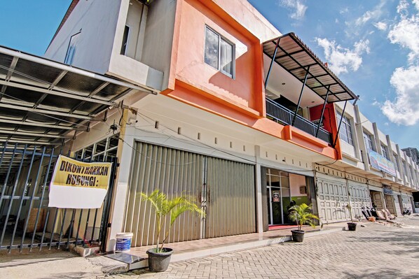 A building with a closed shutter, a balcony, and a sign indicating a business. - Hotel O Rosela House Syariah (Pekanbaru)