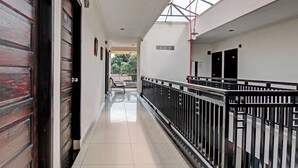 A corridor with a wooden door on the left, a metal railing on the right, and a view of the outdoors through a skylight. - Hotel O Rosela House Syariah (Pekanbaru)