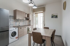 Geladeira, fogão, talheres/pratos/utensílios de cozinha, mesas de jantar