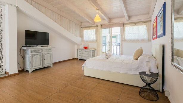 Une chambre à coucher comprenant un lit, une télévision, une commode et un balcon avec une balustrade.