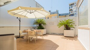 Une terrasse ensoleillée avec une table et des chaises, un grand parasol et des plantes en pot.