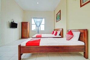 Une chambre d’hôtel avec deux lits en bois, une télévision, une armoire et une fenêtre avec des rideaux légers.