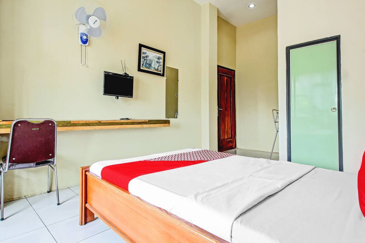 Una habitación de hotel con cama, escritorio, silla, televisión y puerta.