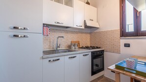 Una cucina con mobili bianchi, un fornello a gas, un lavello e una finestra con persiane in legno.