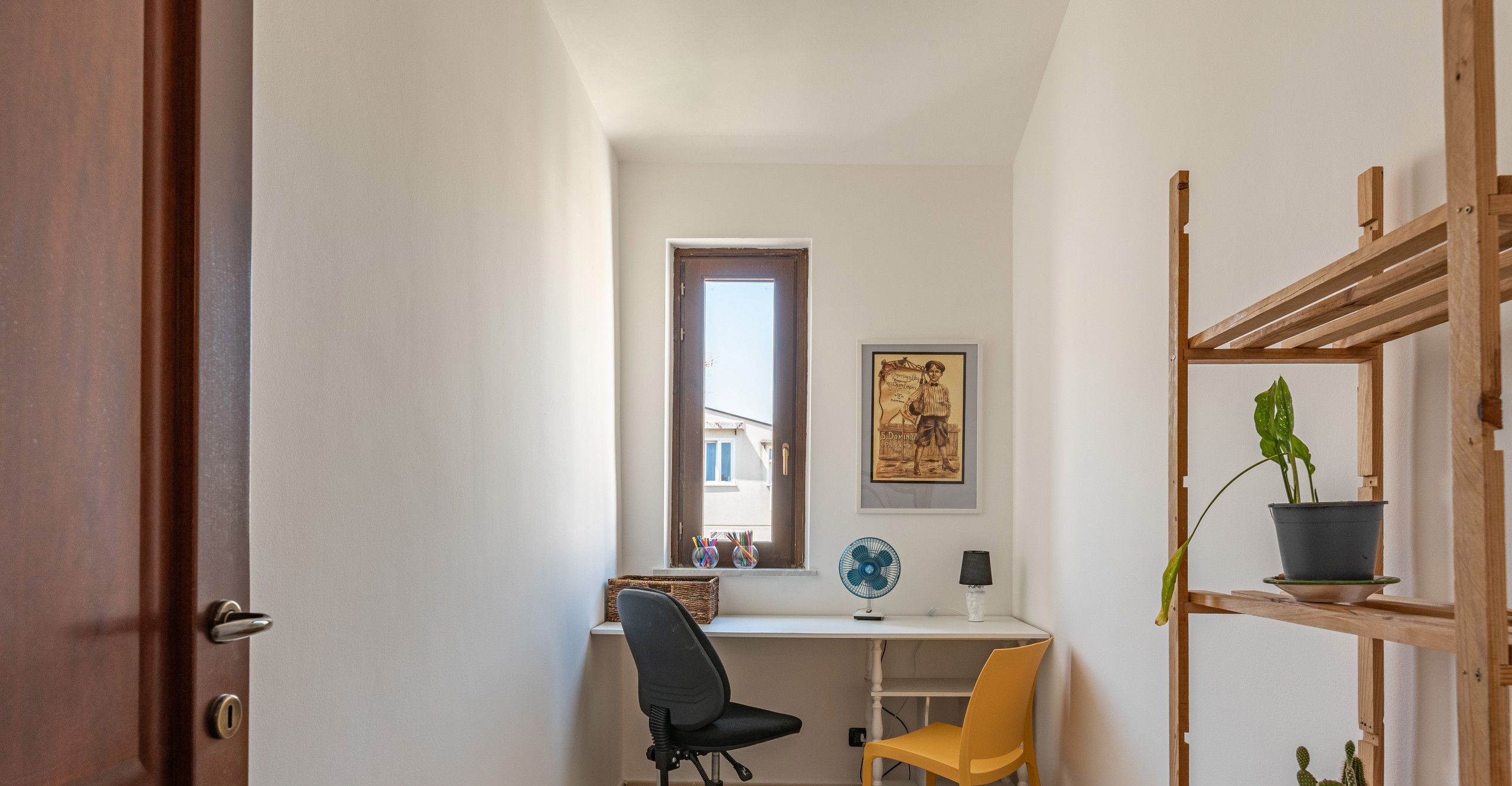 Een functionele kantoorruimte met een bureau, twee stoelen, een raam en een houten plank met planten.