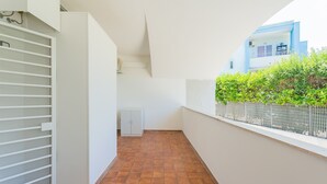 Un couloir étroit au sol carrelé, aux murs blancs et doté d’une porte blanche ornée de barres horizontales.