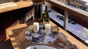 En träveranda med ett bord dukat för en måltid, inklusive ostron och chips, och en flaska vin.