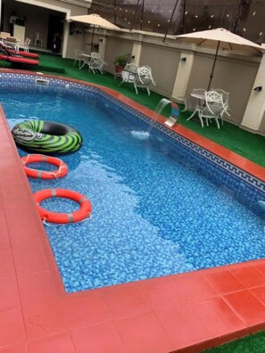 Une piscine avec deux bouées gonflables, entourée de mobilier de jardin et de parasols.