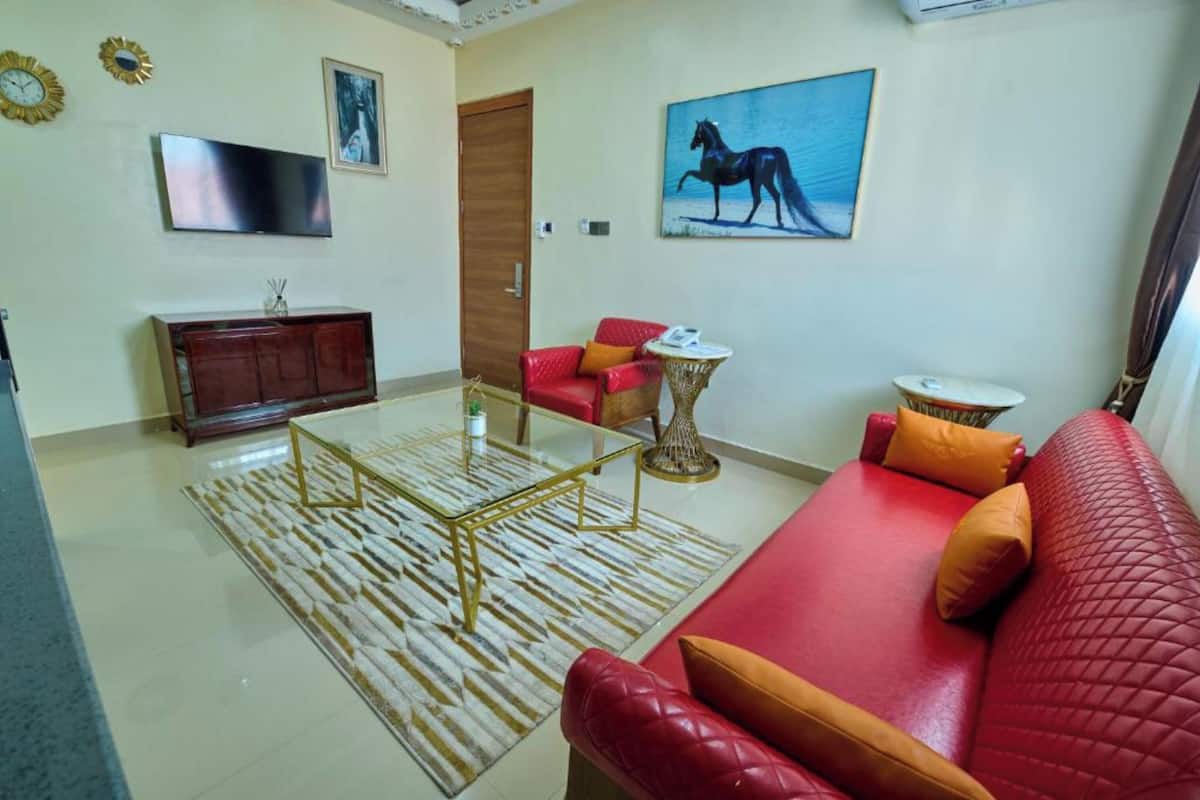 A living room with a red sofa, a glass coffee table, a red armchair, a wooden cabinet, and a painting of a horse.
