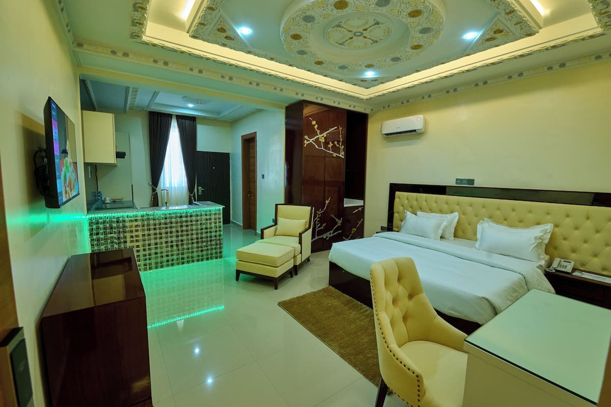A hotel room with a large bed, a desk, a chair, and a small table. There is a TV on the wall and an air conditioning unit above the bed.