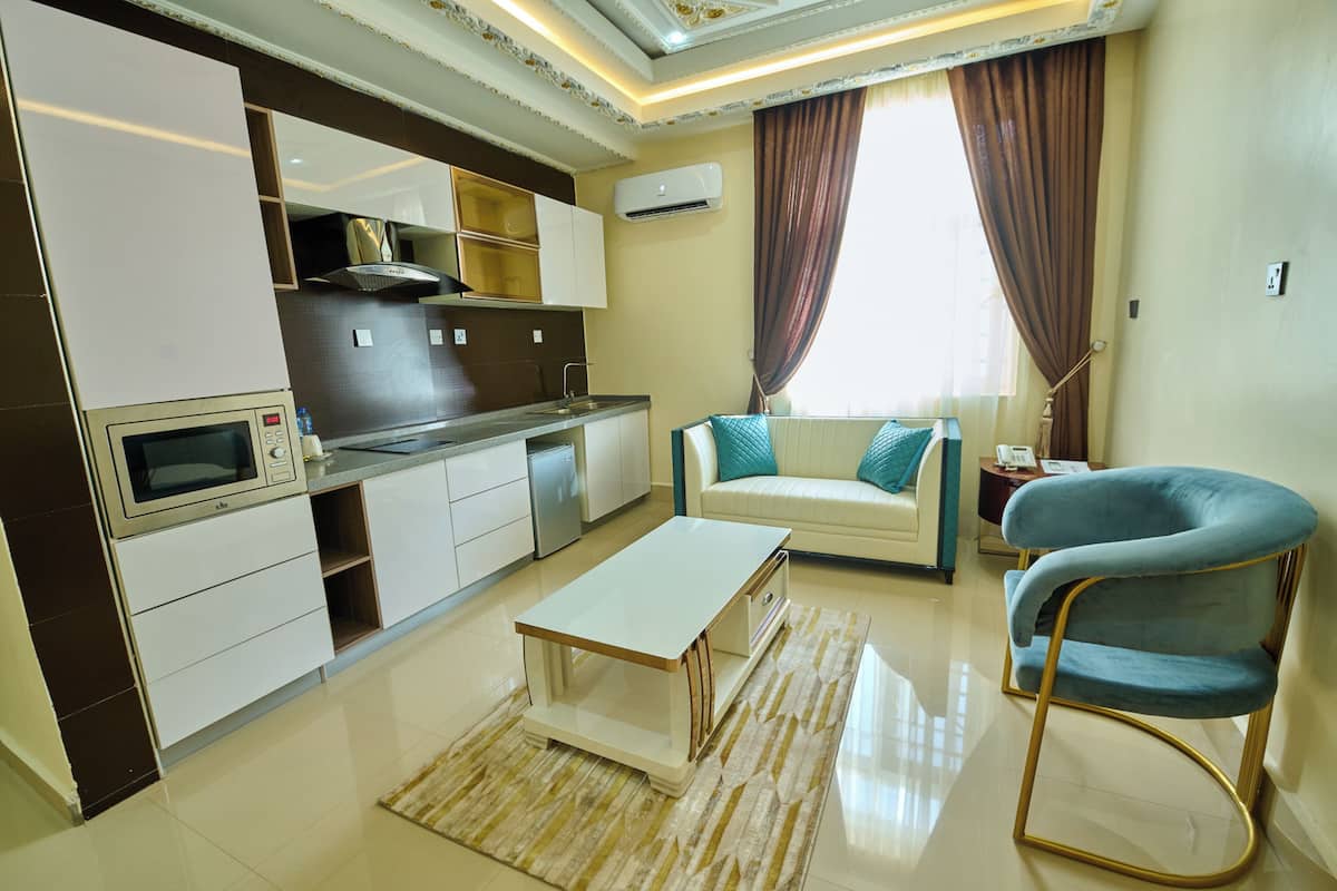 A modern kitchen with white cabinets, a microwave, and a built-in oven. There's a dining area with a white table and a blue chair.
