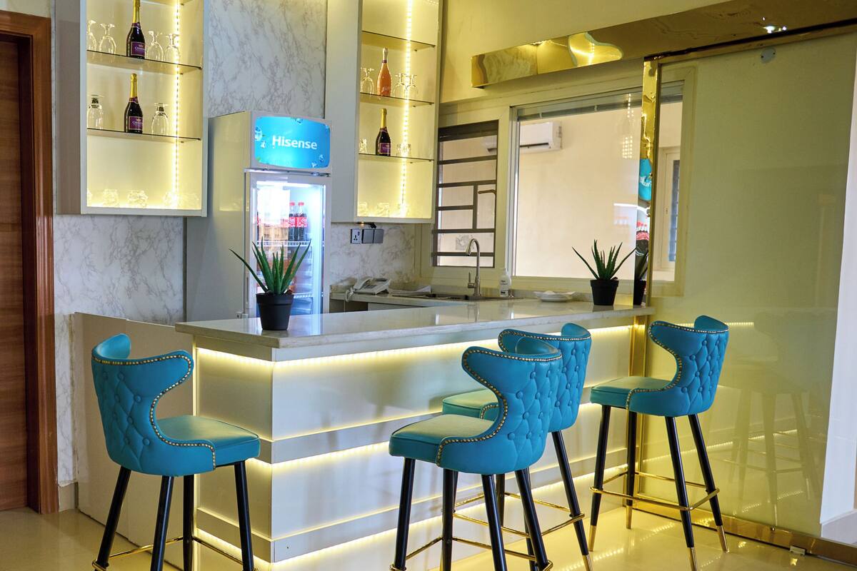 A modern bar area with a marble countertop, blue bar stools, and ambient lighting.