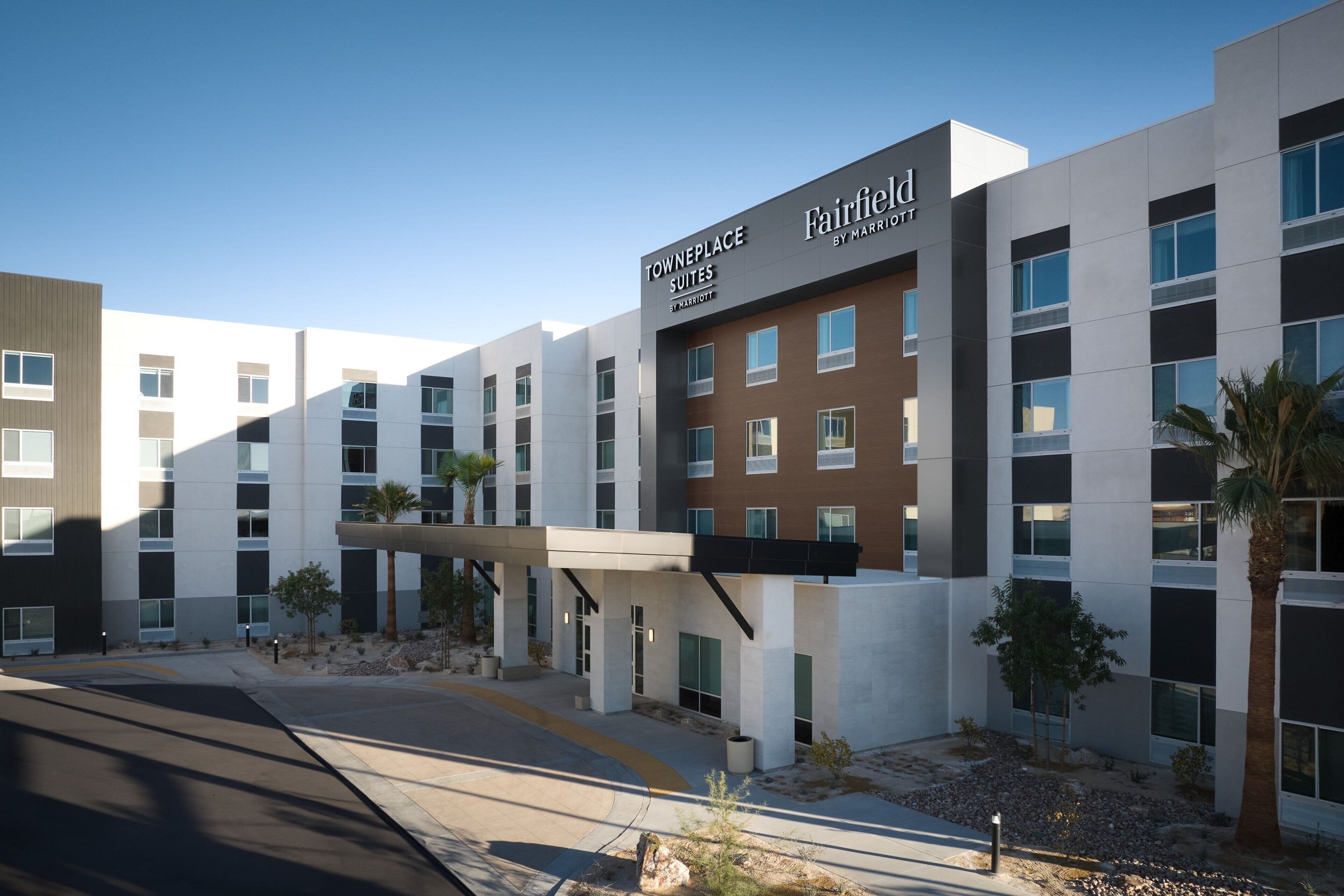 Un hotel moderno con un llamativo letrero de Fairfield by Marriott, que presenta una estructura de varios pisos con fachadas de blanco y marrón, un pasillo cubierto y una zona ajardinada con palmeras.