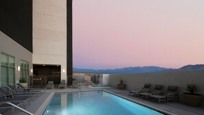A rooftop pool with lounge chairs and a view of mountains.