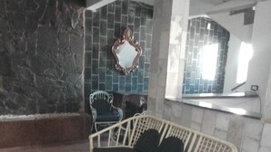 Una habitación con pared de piedra, un espejo, muebles de mimbre y un revoque de azulejos.