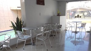Un espacio interior amplio con sillas y mesas de metal, suelo de baldosas y una planta en maceta.
