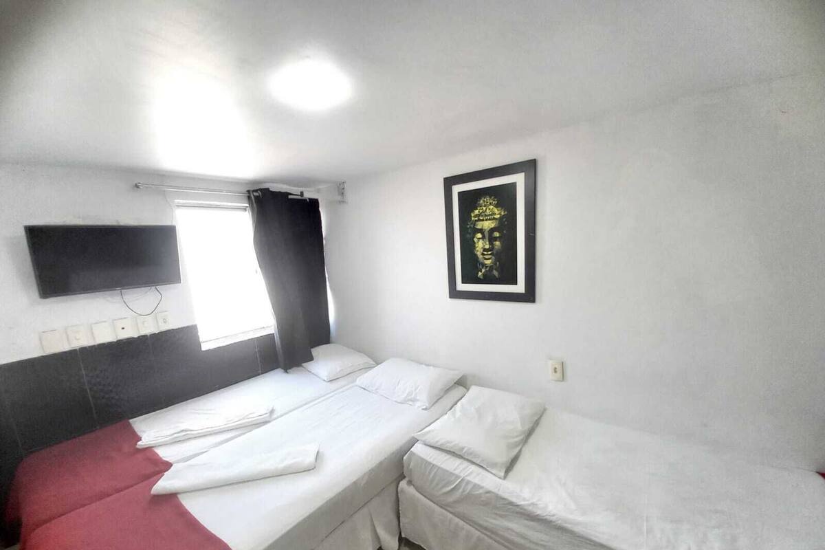 Ein Zimmer mit einem Bett, einem an der Wand montierten Fernseher und einem gerahmten Kunstwerk.