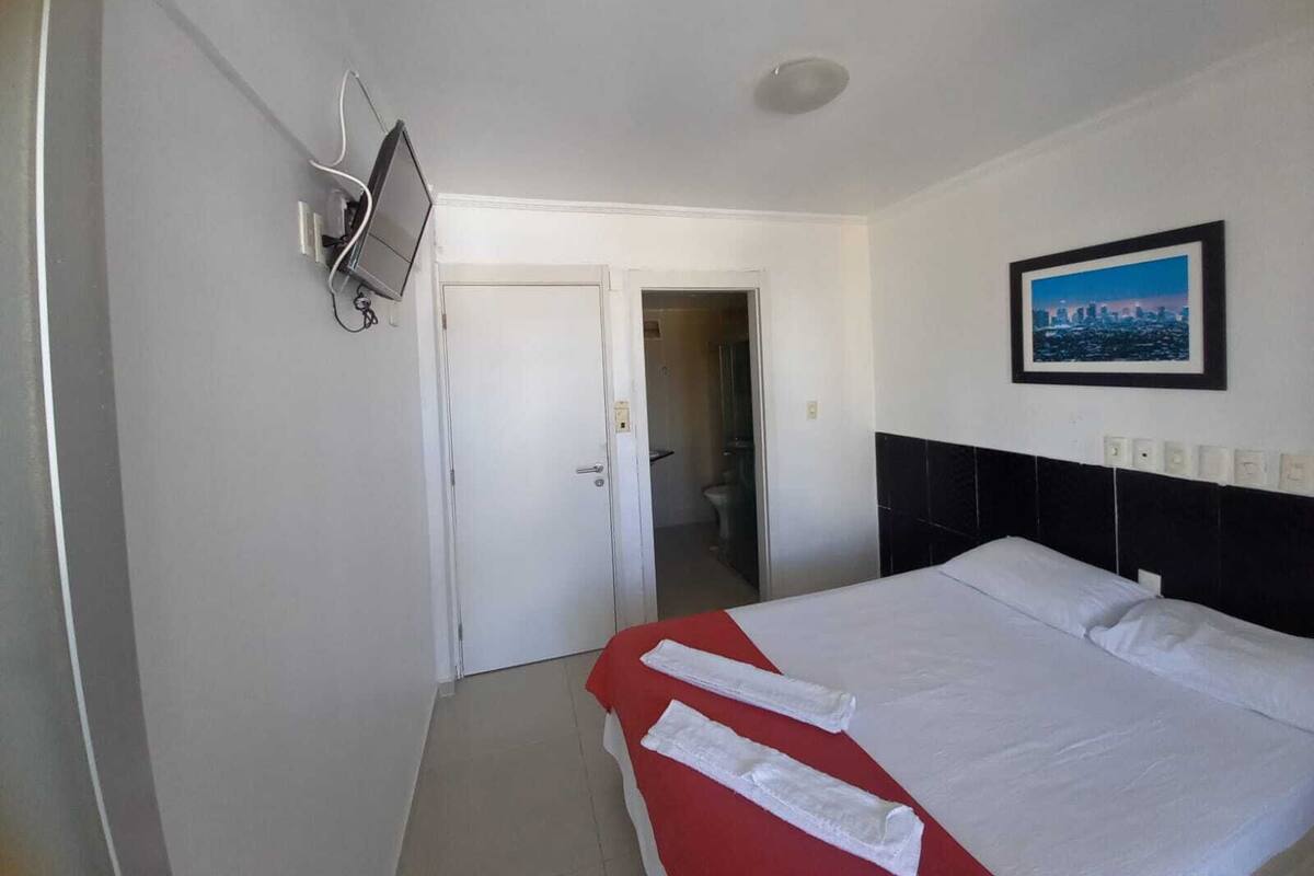 Ein Hotelzimmer mit einem Bett, einem an der Wand befestigten Fernseher, einem gerahmten Bild und einer Tür zu einem Badezimmer.