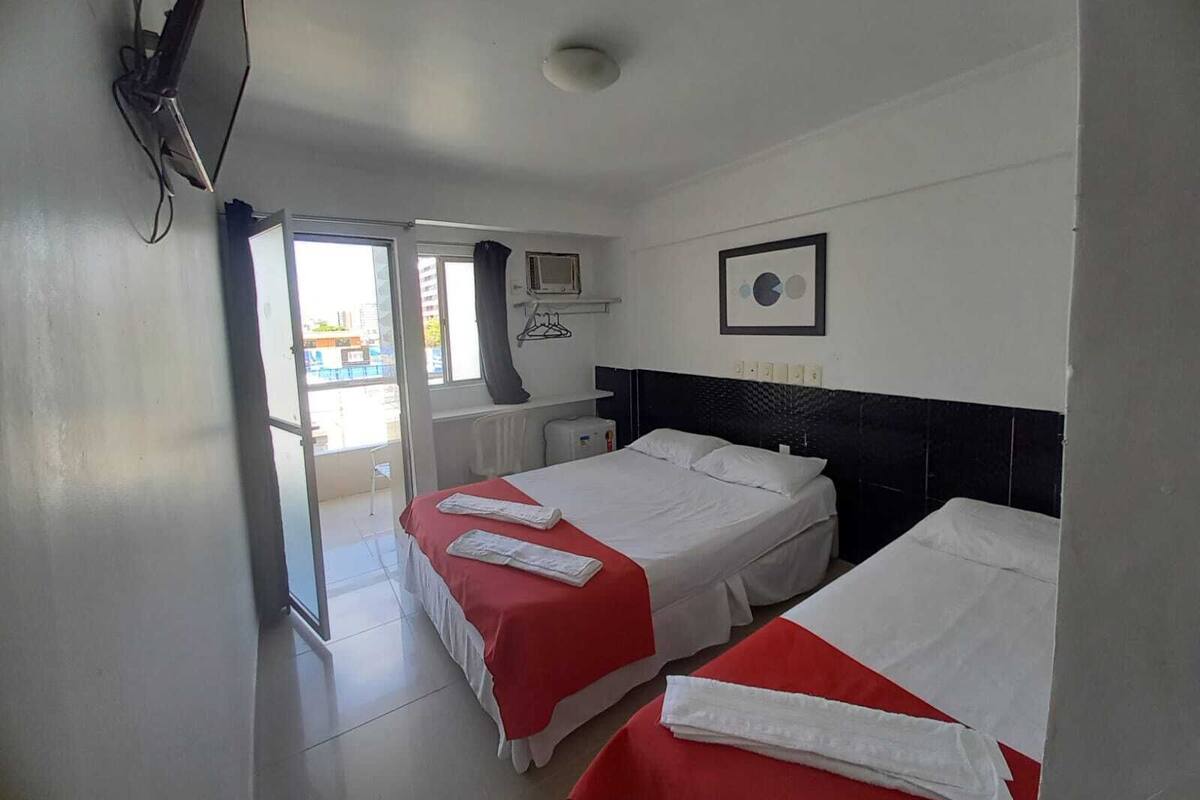 Ein Hotelzimmer mit zwei Betten, einem Fernseher, einem Fenster und Blick nach draußen.