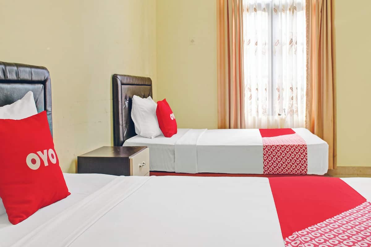 A hotel room with two beds, a nightstand, and a window with curtains.