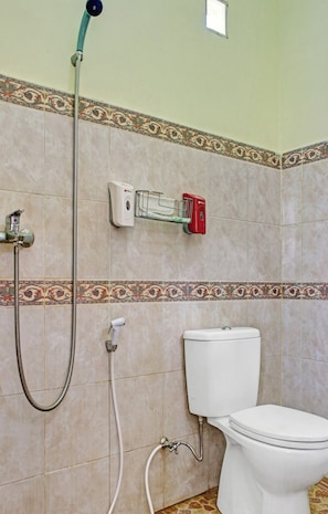 Un baño con inodoro, ducha con manguera y dispensador de jabón en la pared.